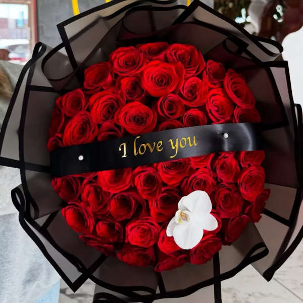 Bouquet of red roses wrapped in black paper with a white orchid accent