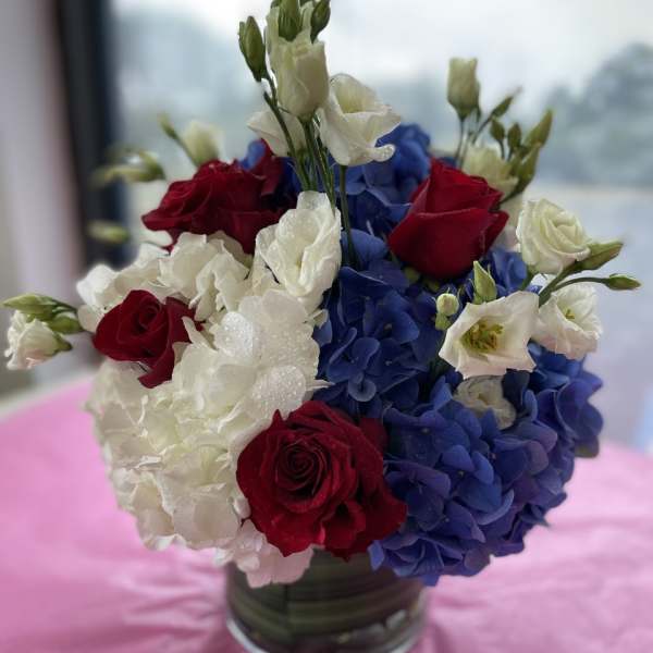 Red roses and white blooms arranged with blue hydrangeas in a glass vase