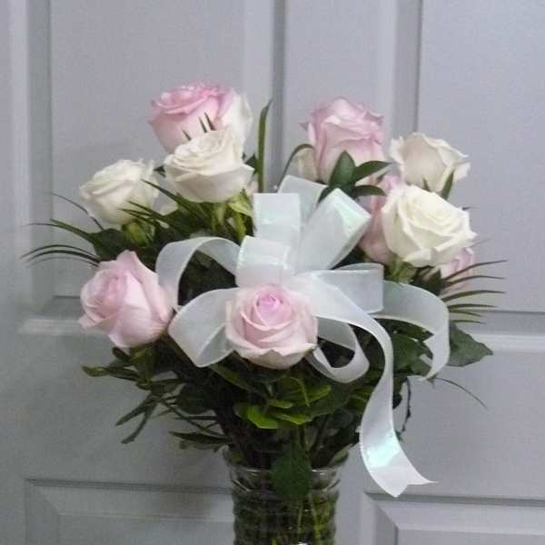 Pink and white roses arranged in a glass vase with a white ribbon