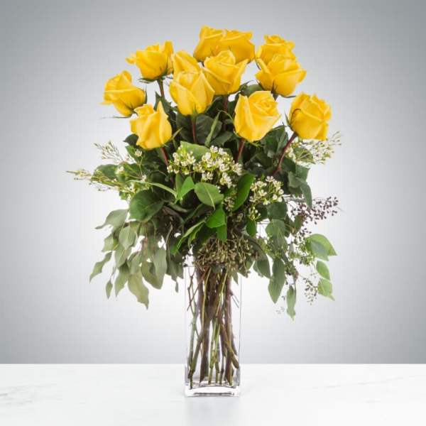Yellow roses arranged in a clear glass vase with greenery