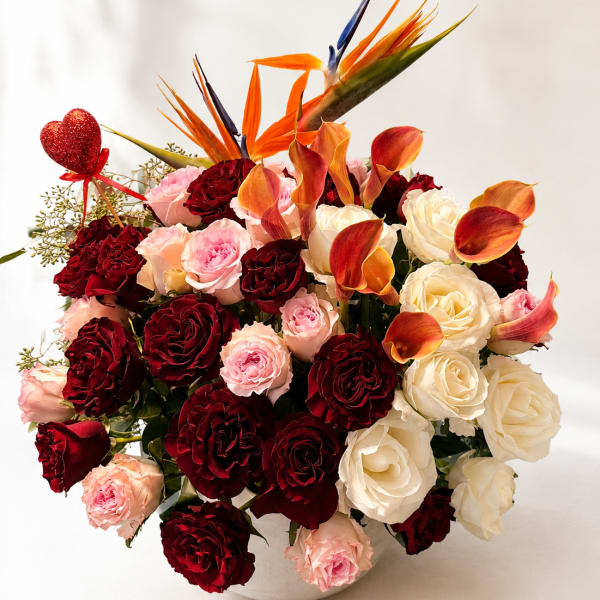 Bouquet of red, pink, and white roses with orange calla lilies in a white vase