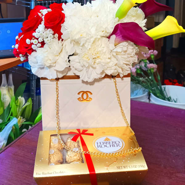 Flower arrangement with red roses, white carnations, and yellow calla lilies on a chocolate box