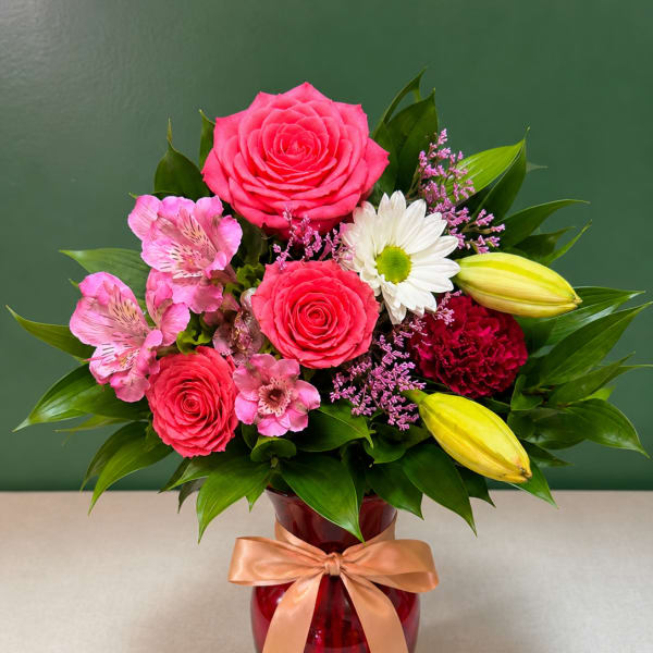 Pink roses and lilies arranged in a red vase with a ribbon