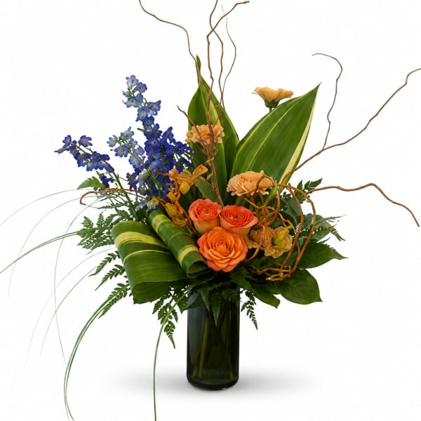 Orange roses and blue flowers in a tall glass vase with curly branches