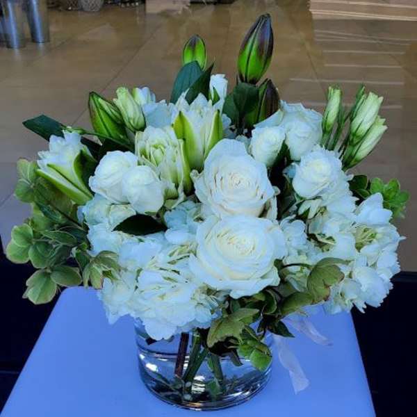 Low glass vase of white roses, lilies, and hydrangeas in a rounded arrangement