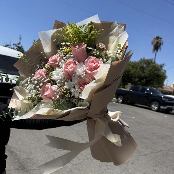 Handheld bouquet of pink roses and white flowers wrapped in beige paper