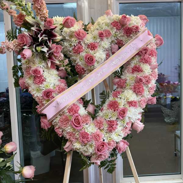 Heart-shaped pink and white floral standing spray with a ribbon across it