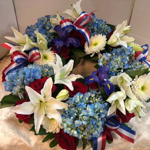Floral wreath with blue hydrangeas, white lilies, red roses, and ribbon bows