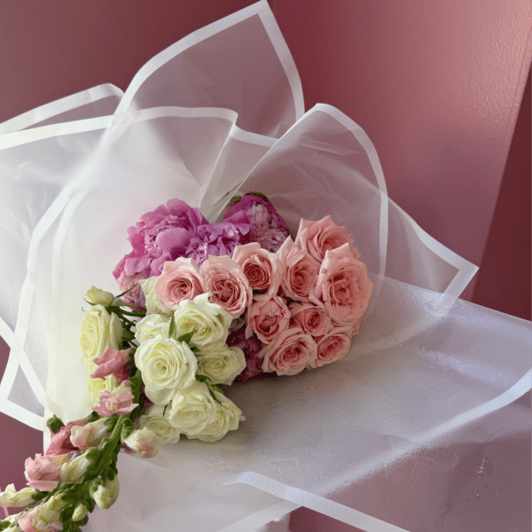 Bouquet of pink and cream roses with purple blooms wrapped in white paper