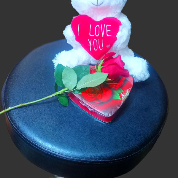 White teddy bear holding a pink heart with a red rose on a stool