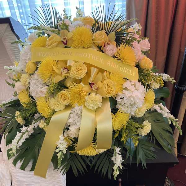 Yellow and white funeral spray with ribbon on a casket