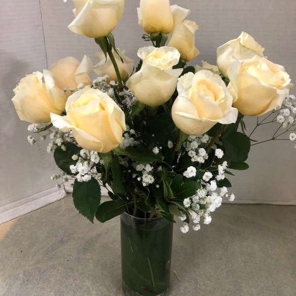 Cream roses arranged in a clear glass vase with small white filler flowers