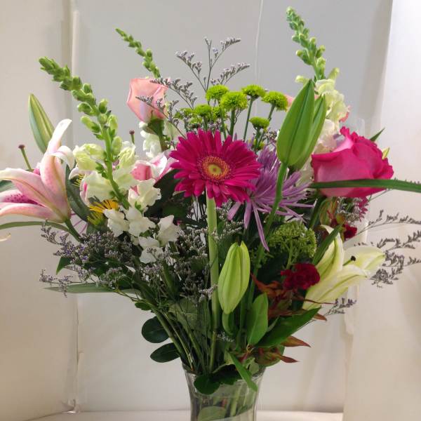 Mixed bouquet of lilies, roses, and daisies in a clear glass vase