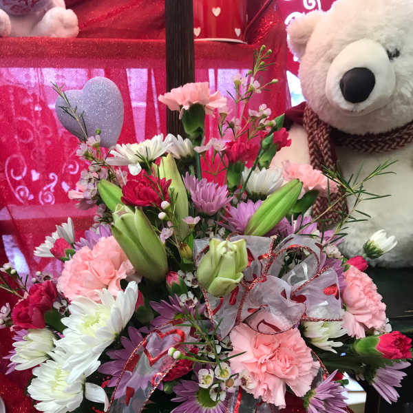 Mixed pink and white flower arrangement in a glass vase with a teddy bear