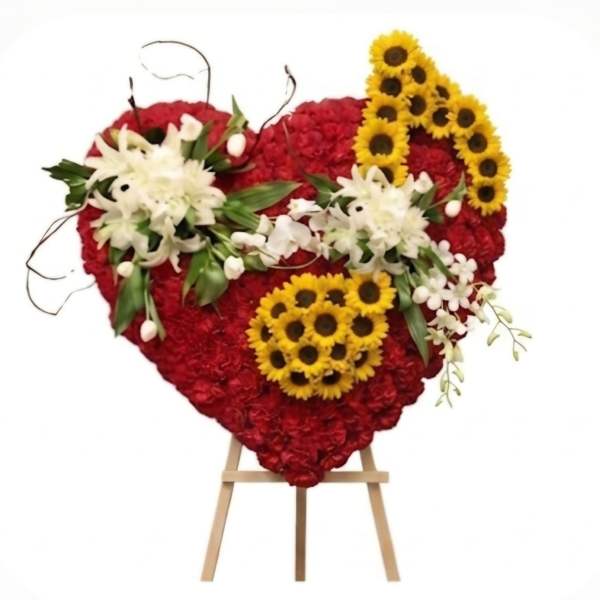 Heart-shaped red floral arrangement with white lilies and yellow sunflowers on an easel