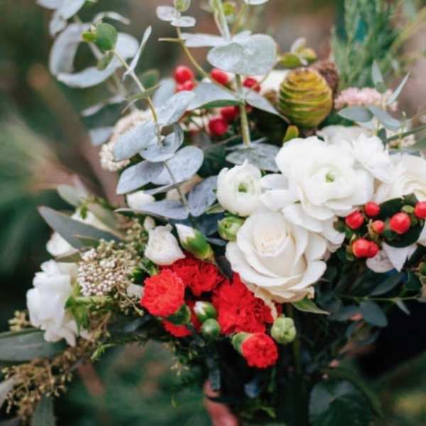 Hand-tied bouquet with white roses, red carnations, berries, and eucalyptus stems.