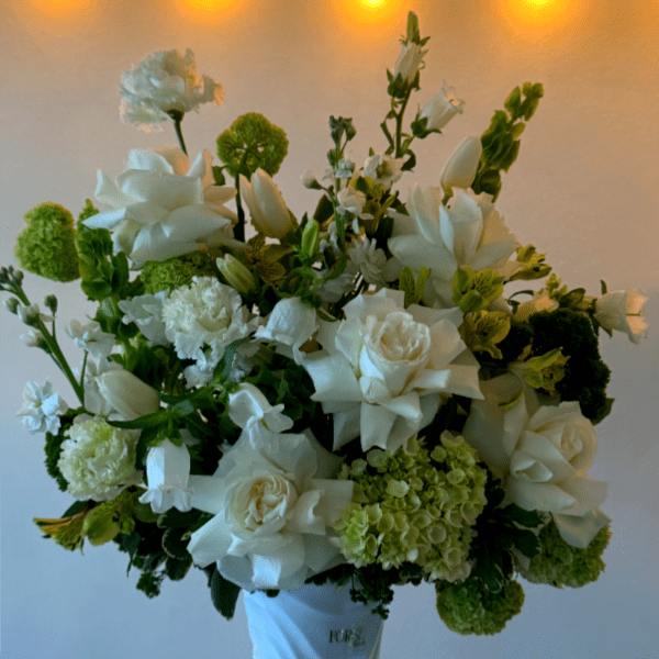White floral arrangement in a white vase with green accents