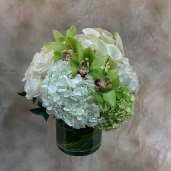 White floral arrangement in a dark glass vase with green accents