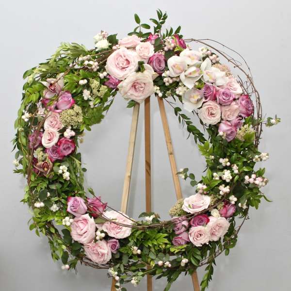 Circular floral wreath with pink and white roses on a wooden stand