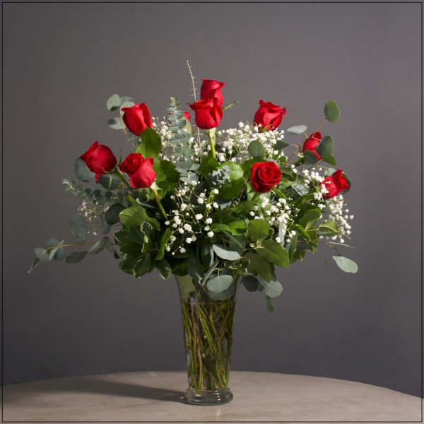 Red roses arranged in a clear glass vase with white filler flowers