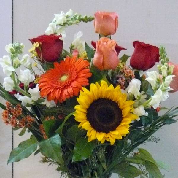 Mixed bouquet of roses, gerbera daisies, and sunflowers in a glass vase