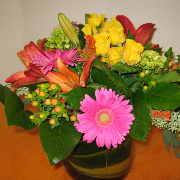 Mixed bouquet of yellow roses, pink gerbera daisies, and lilies in a glass vase