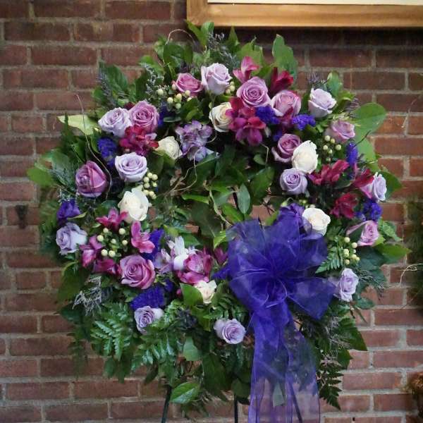 Large floral wreath with purple roses and a sheer purple bow on a stand