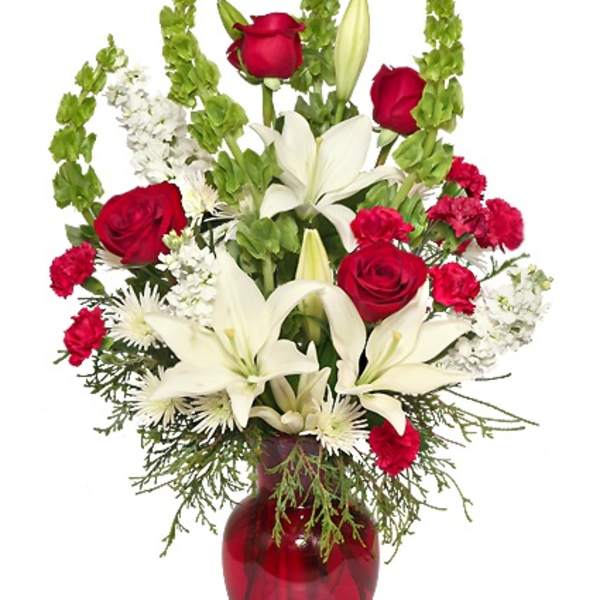 Tall arrangement of red roses, red carnations, and white lilies in a red glass vase