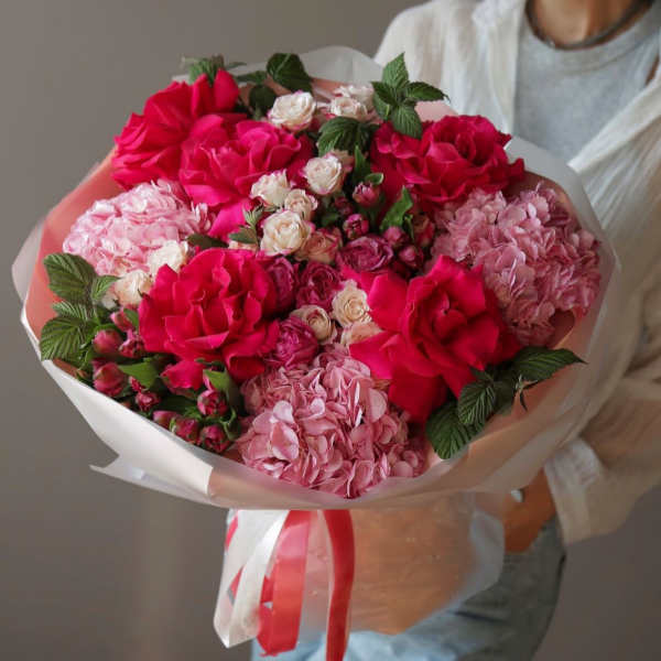 Bouquet of pink hydrangeas, roses, and small spray roses wrapped in white paper