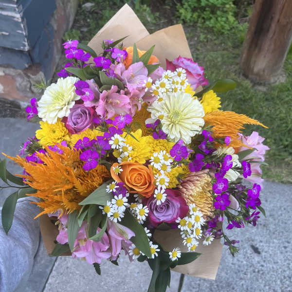 Mixed bouquet with roses, daisies, and bright orange accents in brown paper