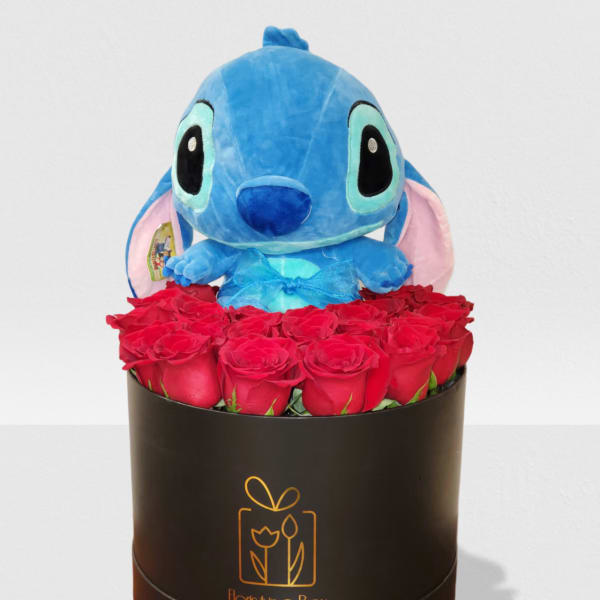 Blue plush toy sitting above a cluster of red roses in a black hat box