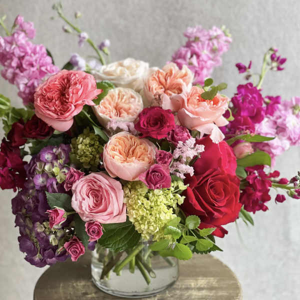 Pink and red roses arranged in a clear glass vase with purple blooms
