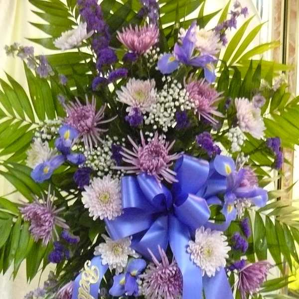 Purple and white funeral spray with a blue ribbon and palm fronds