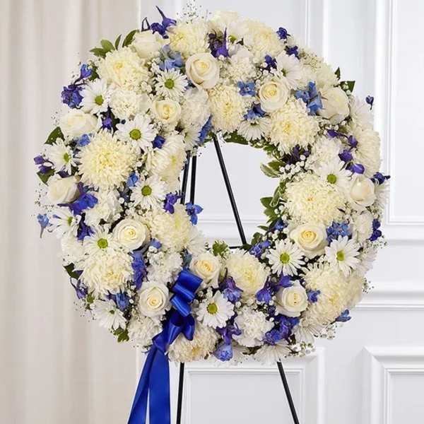 White floral wreath with blue accents on a stand