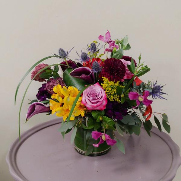 Mixed bouquet with pink roses, purple calla lilies, and yellow flowers in a glass vase