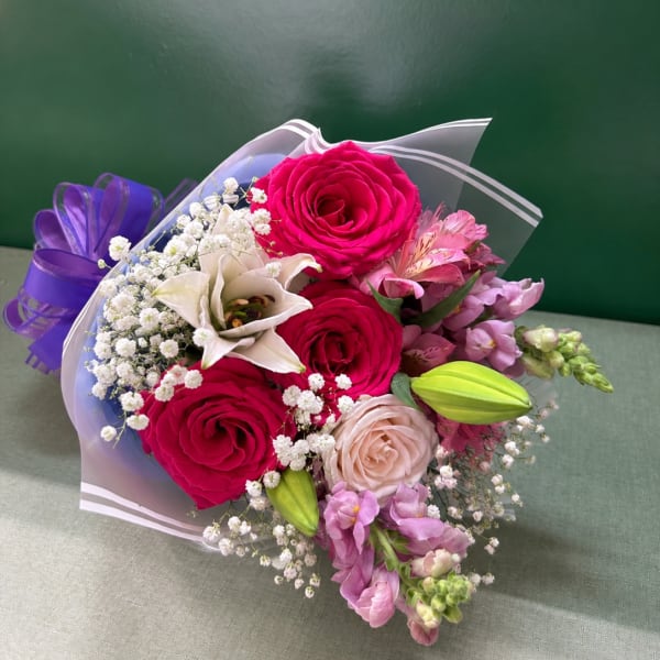 Bouquet of pink roses, white lily, and purple flowers wrapped in clear paper