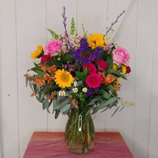 Mixed bouquet of roses, sunflowers, and daisies in a glass vase
