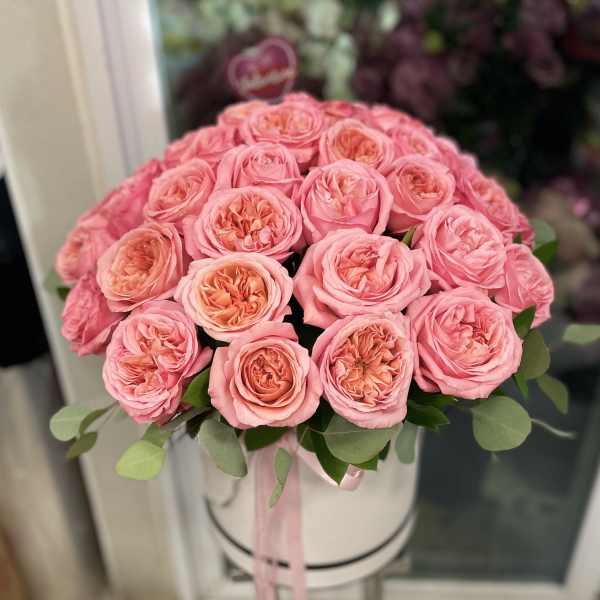 Pink roses arranged in a round white hat box with a ribbon