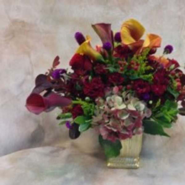 Mixed bouquet with calla lilies and dark purple flowers in a square vase