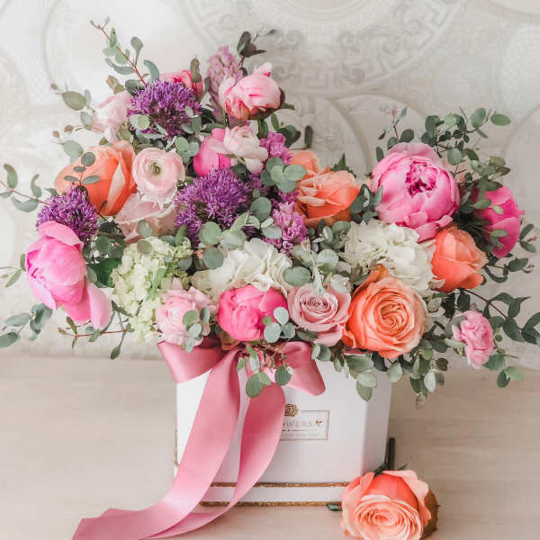 Pink and peach flower arrangement in a white box with a ribbon