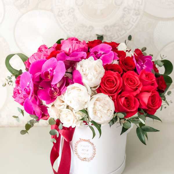Pink and red floral arrangement in a white hat box with ribbon