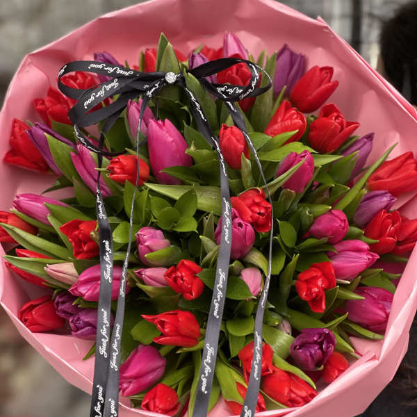 Bouquet of red and pink tulips wrapped in pink paper with a black ribbon