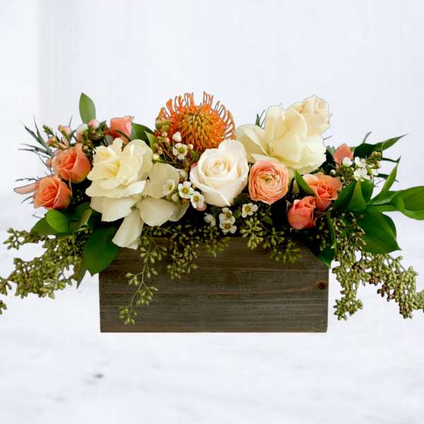 Mixed floral arrangement in a wooden box with peach, cream, and orange blooms