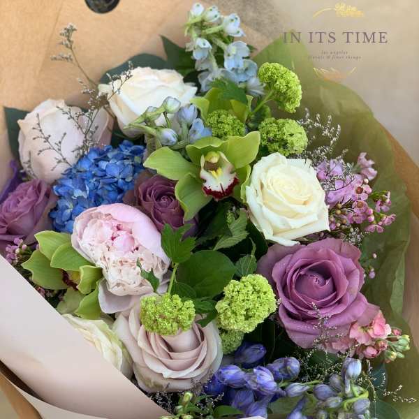 Bouquet of roses, hydrangea, orchids, and green blooms in paper wrap