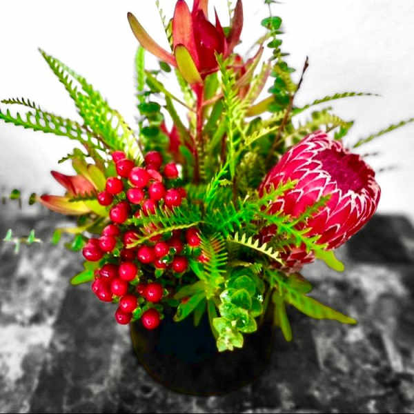Bright tropical flower arrangement in a black vase with red berries