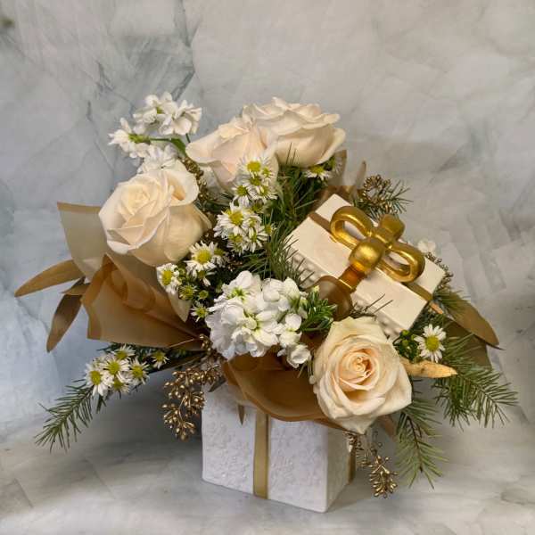 Cream roses and small white flowers arranged with a gift box and gold ribbon