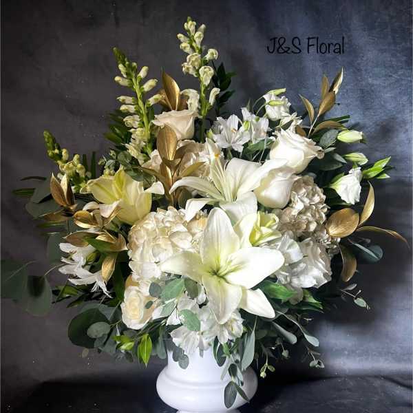 White floral arrangement in a white pedestal vase with gold foliage accents