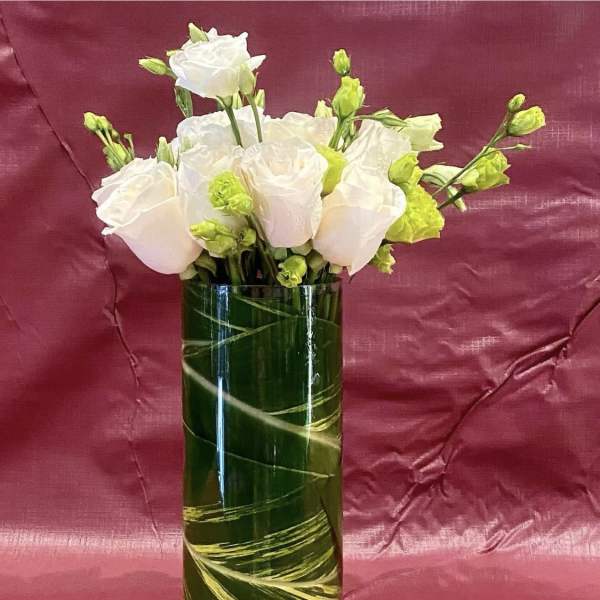 White roses and green buds arranged in a tall glass vase.