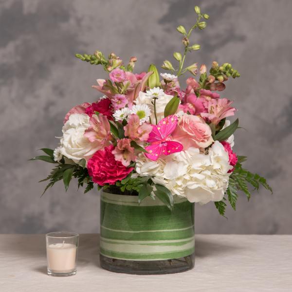 Pink and white mixed flower arrangement with butterfly pick in a striped green glass vase