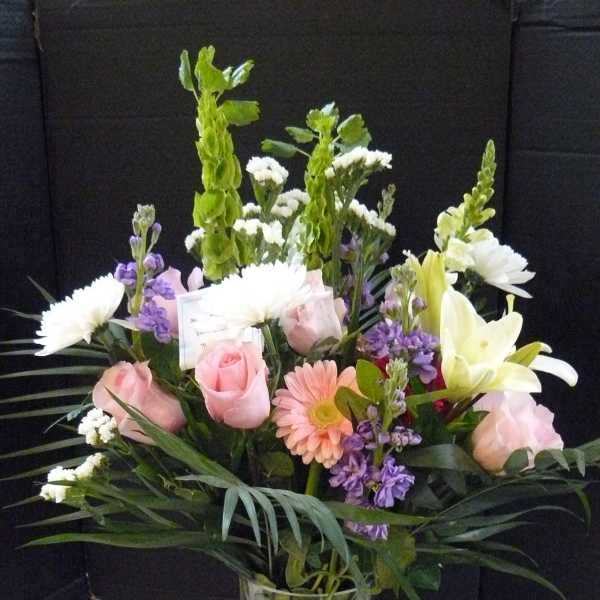 Mixed bouquet of pink roses, white lilies, and purple flowers in a glass vase